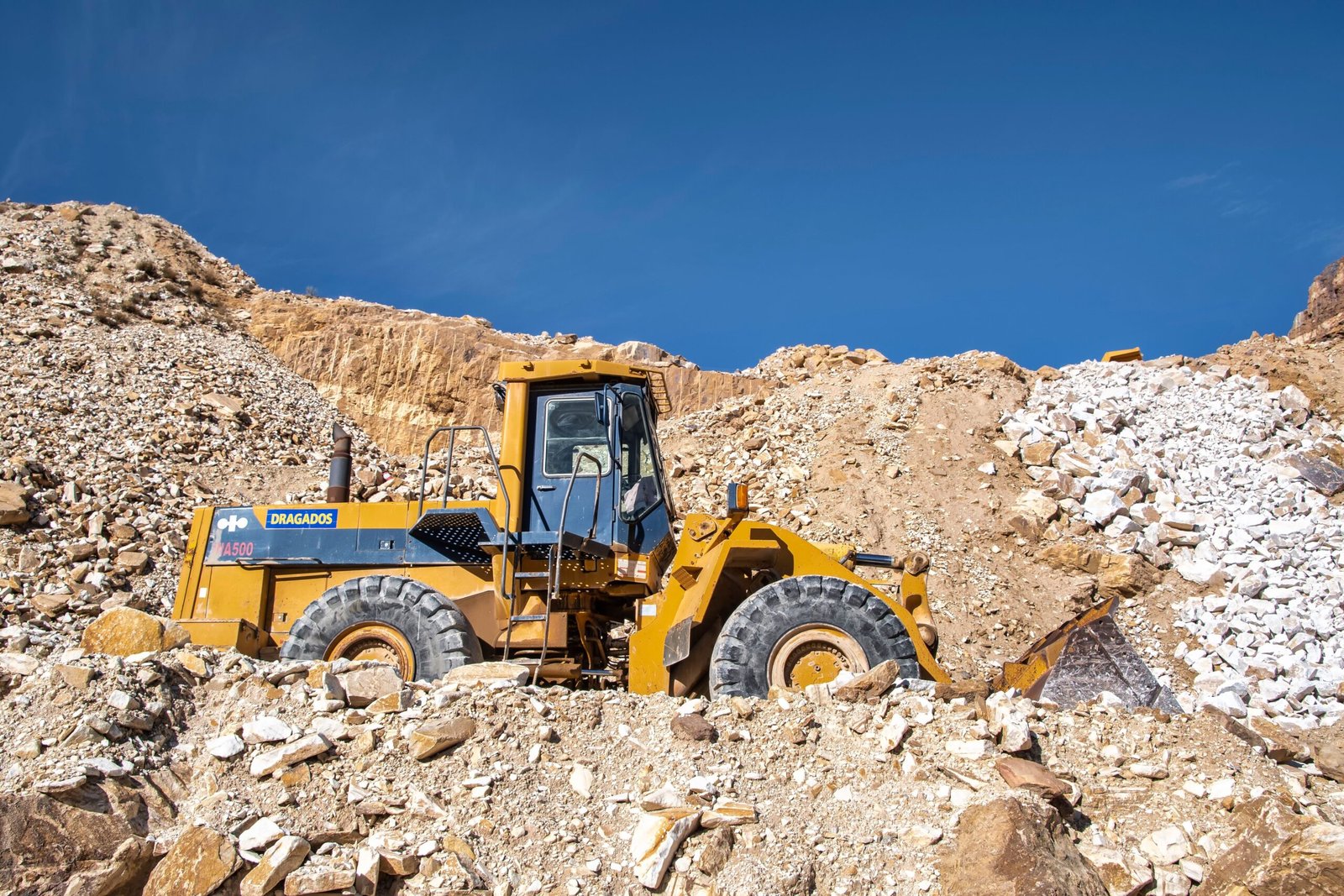 Home Industrial bulldozer operating in a sunny quarry with rocky terrain.