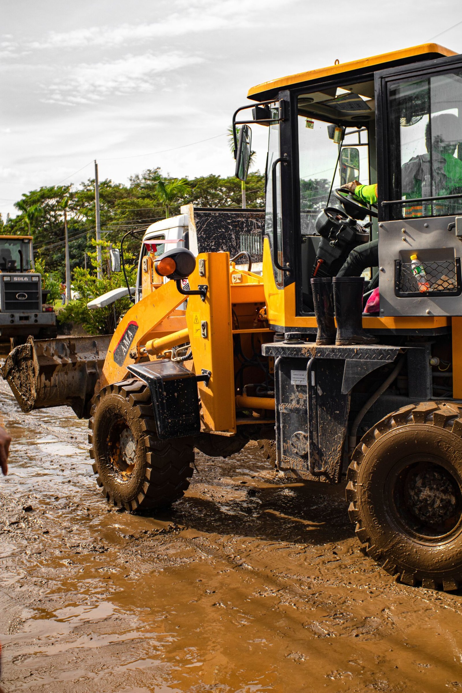 Home Back view of anonymous workman in modern loader with bucket on wet roadway with mud on sunny day